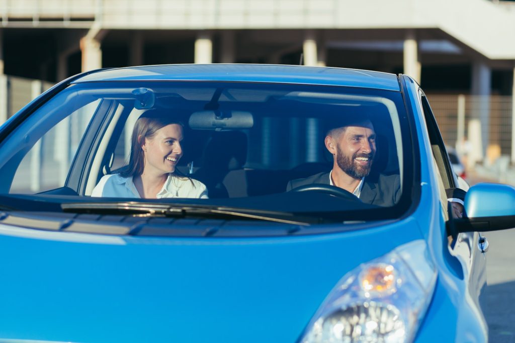 Male driving instructor and female driving school student sitting together in car smiling, learning