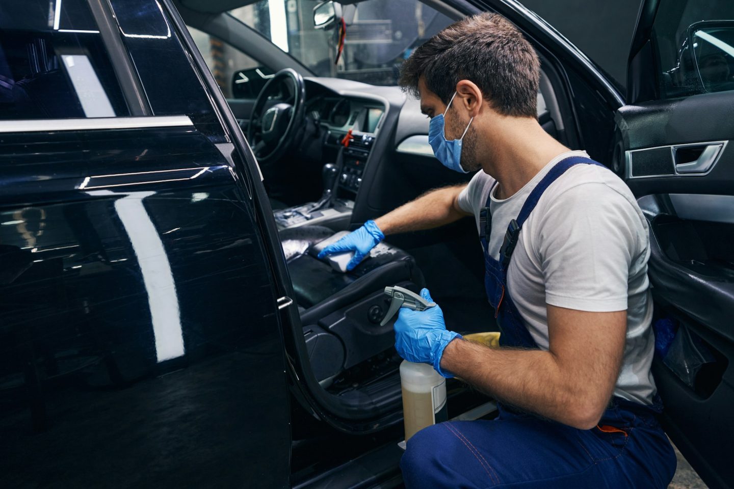 Male wiping seat clean in black car during detailing