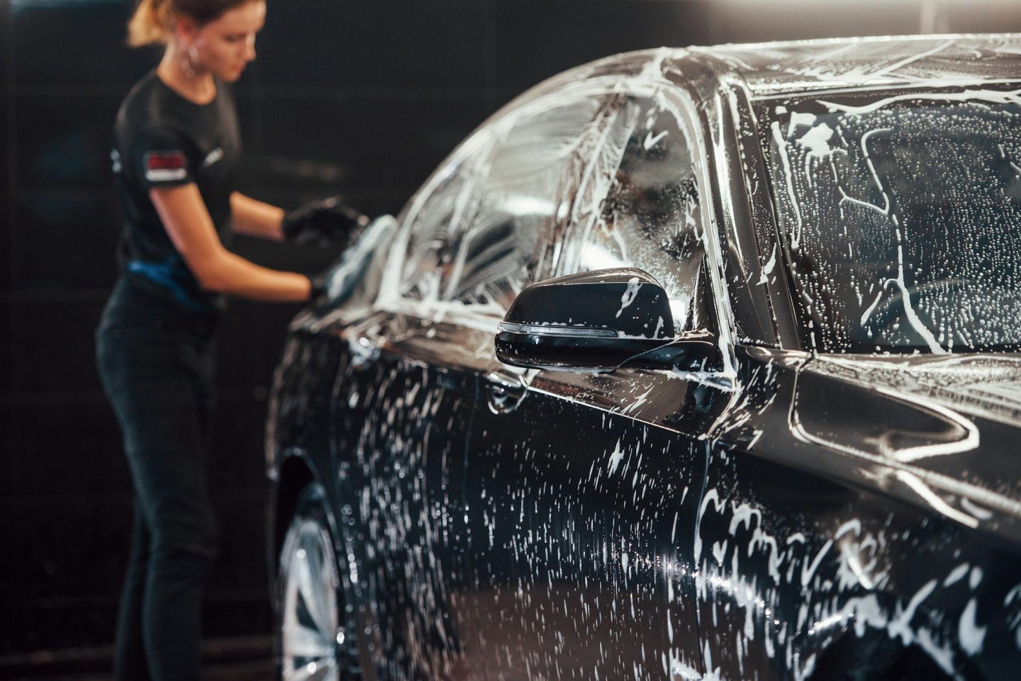 Modern black automobile get cleaned by woman inside of car wash station